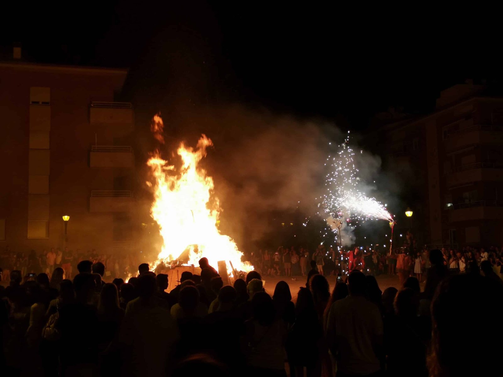 Large bonfire with diables and firework banners during Sant Joan celebration in a Barcelona square at night