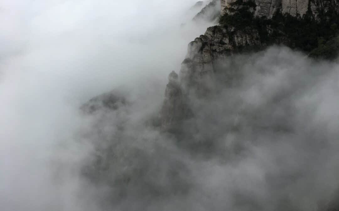 Montserrat mountain enveloped by clouds, appearing to rise into the sky.