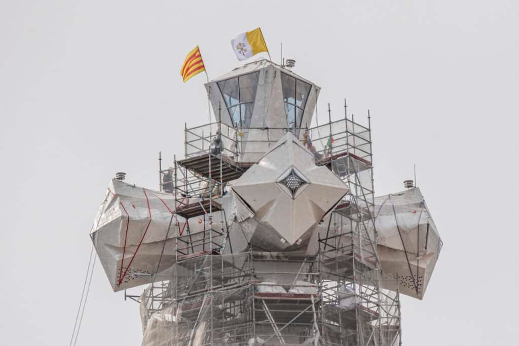 Completed cross crowning the Tower of Jesus Christ at the Sagrada Familia with the Catalan flag and the Vatican flag