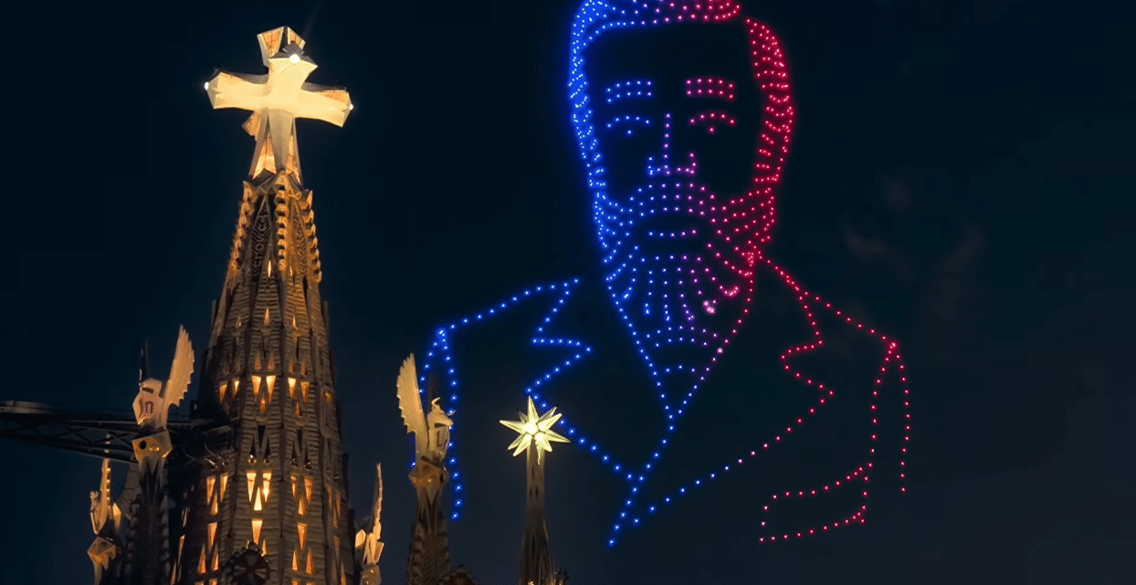 Drone portrait of Antoni Gaudí appearing beside the illuminated Tower of Jesus.
