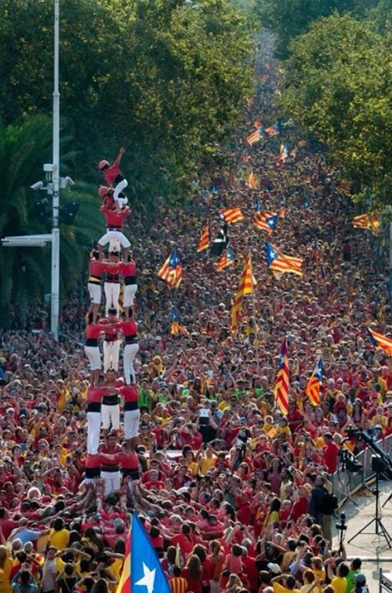 Human tower (castell) rising amid a massive crowd with Catalan flags during La Diada in Barcelona.