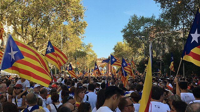Crowd under tree-lined streets waving Catalan flags during La Diada.