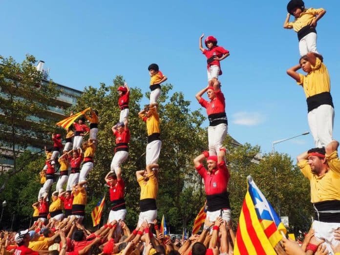 Multiple teams of castellers building human towers during La Diada celebrations in Barcelona with Catalan flags.