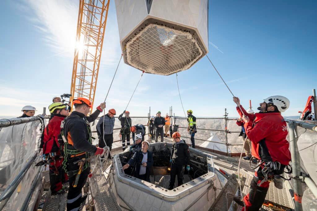 Construction workers guiding the upper arm of the cross into position on the Tower of Jesus Christ at the Sagrada Familia