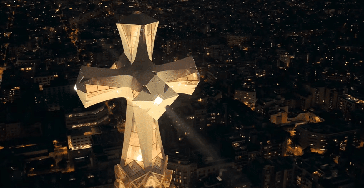Close-up view of the illuminated cross atop the Tower of Jesus at the Sagrada Familia overlooking Barcelona at night.