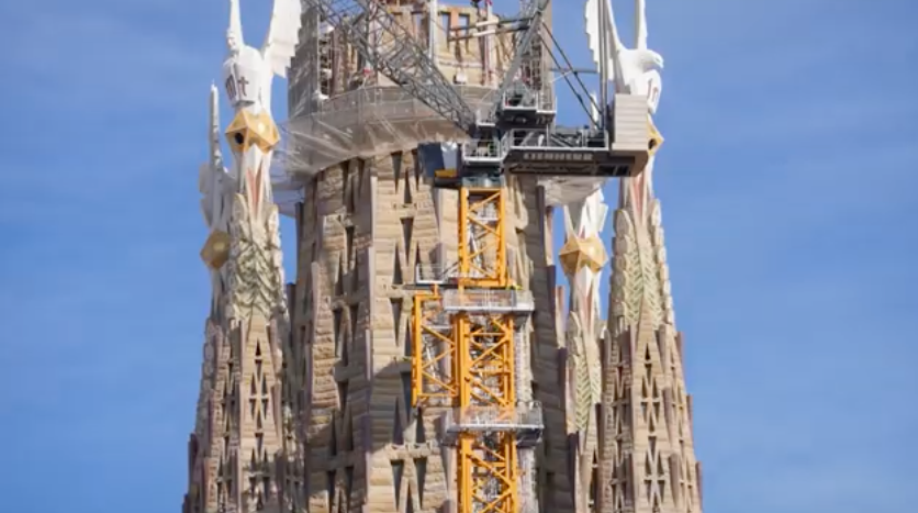 Close-up view of the upper section of the Jesus Tower at the Sagrada Família, showing the angel sculptures and yellow crane during construction in 2025.